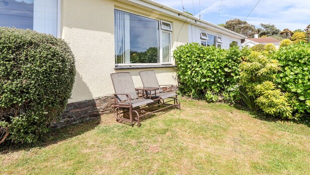 Une maison de plain-pied dotée d’une grande fenêtre, d’une cheminée et d’un petit patio avec deux chaises.