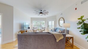 A spacious living room with a grey sofa, a television, and a dining area with a table and chairs. - Serene 5th floor Villa with Two Balconies! (Hilton Head)