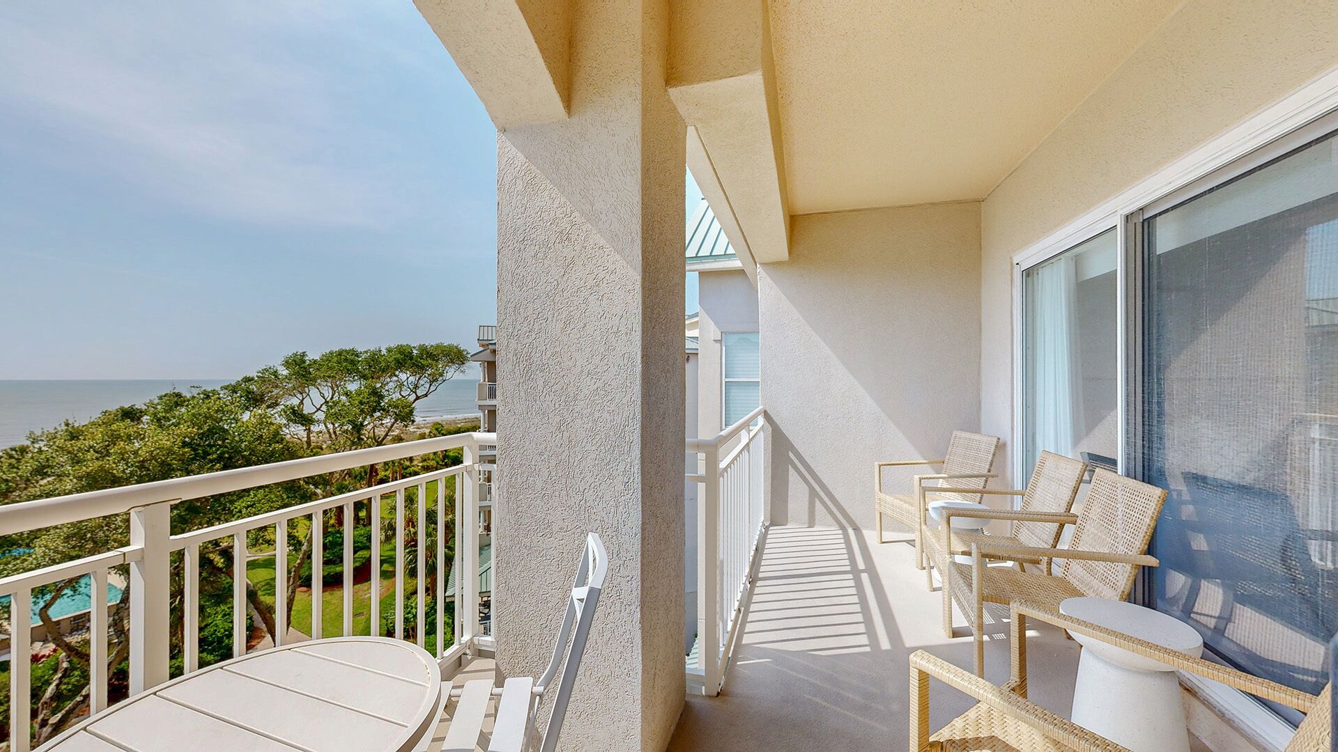 A balcony with a view of the ocean, wicker furniture, and a white railing.
