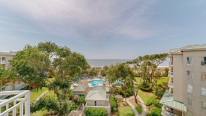 A residential area with a swimming pool, trees, and a view of the ocean. - Serene 5th floor Villa with Two Balconies! (Hilton Head)