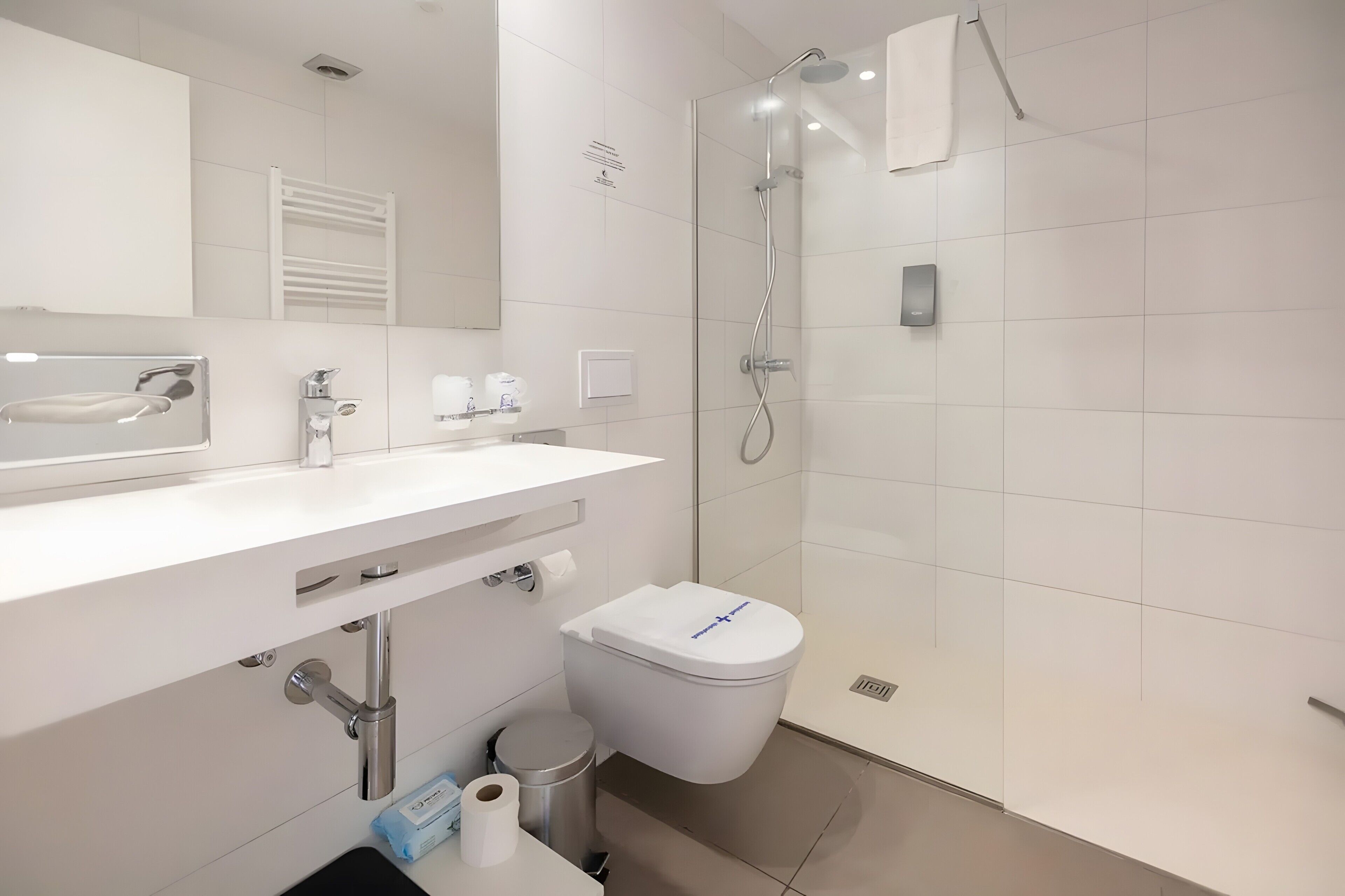 A modern bathroom with a white sink, mirror, toilet, and shower.