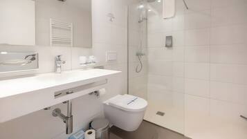 A modern bathroom with a white sink, mirror, toilet, and shower.