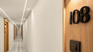 Un couloir avec une porte en bois portant le numéro « 108 », un interrupteur et un luminaire fixé au mur.
