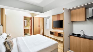 Une chambre d’hôtel moderne équipée d’un lit, d’une petite kitchenette, d’un téléviseur fixé au mur et d’une armoire en bois.