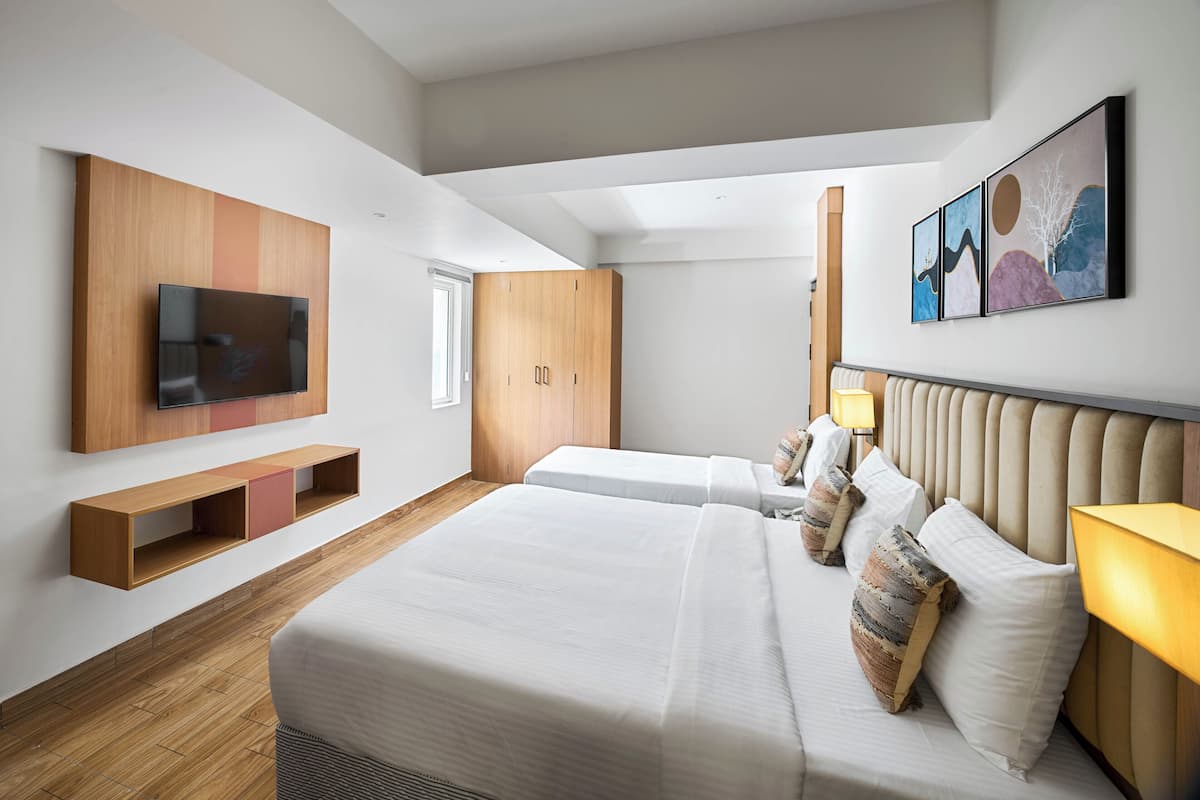 A modern hotel room with a large bed, a TV mounted on the wall, wooden shelving, and artwork on the wall.