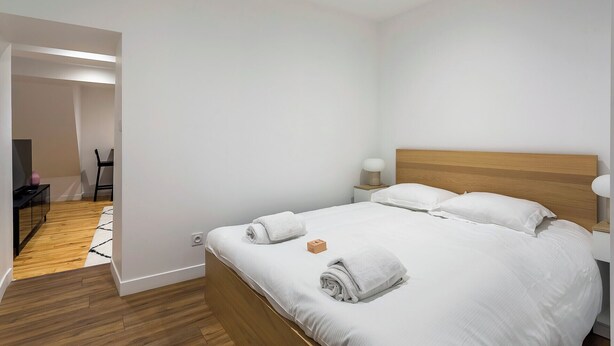 Une chambre d’hôtel moderne avec une tête de lit en bois, du linge de lit blanc et un lit parfaitement fait, agrémenté de serviettes roulées.
