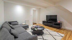 Un salon moderne avec un canapé d’angle, un meuble de rangement noir et un téléviseur à écran plat.