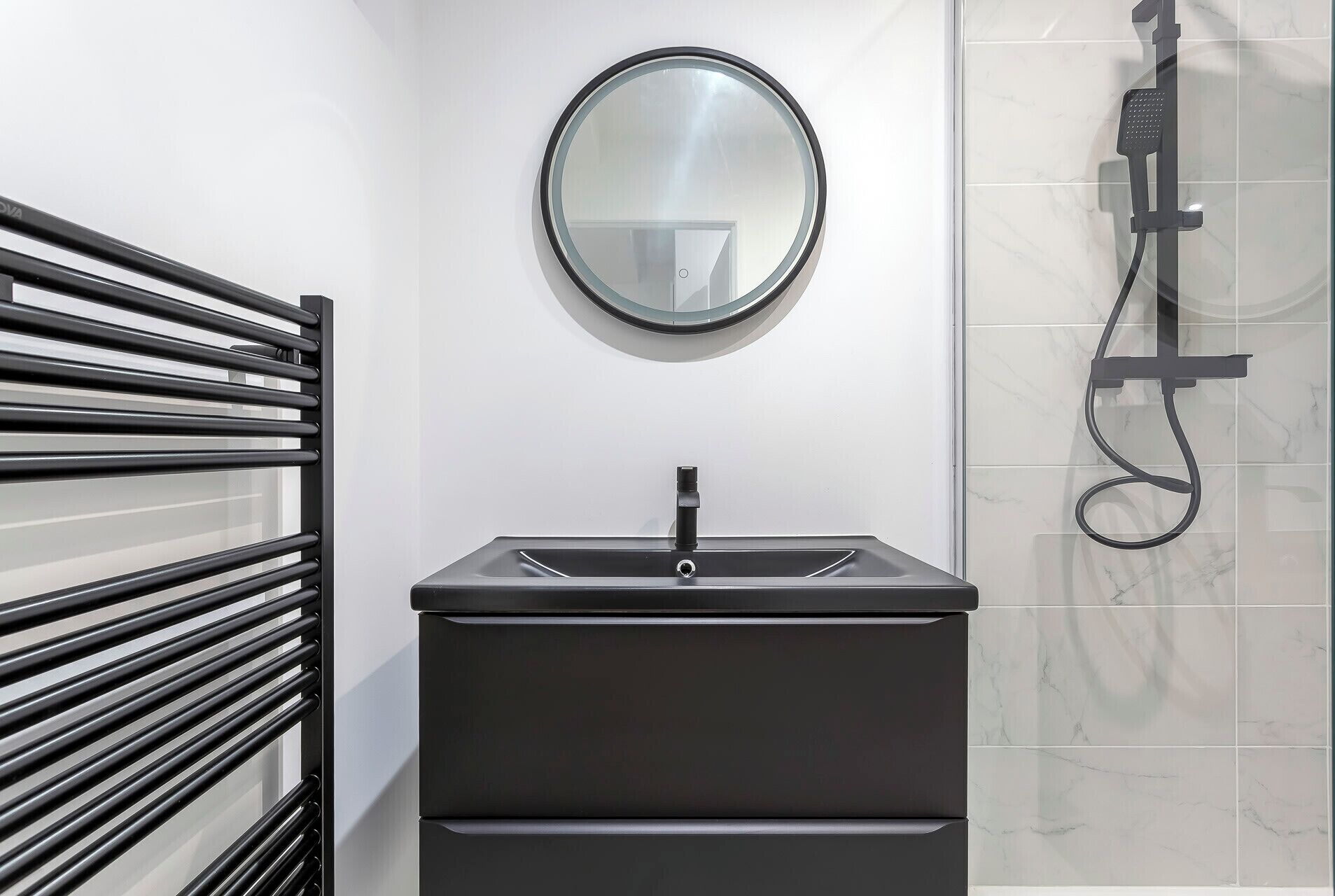 Een moderne badkamer met een zwart wastafel, een ronde spiegel en een handdouche.