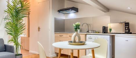 A modern kitchen with a dining area, a white refrigerator, and a potted plant.