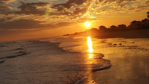 Un coucher de soleil sur une plage, avec des vagues et un ciel dégagé.