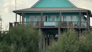 Un bâtiment turquoise doté d’un balcon, d’un drapeau et d’une enseigne indiquant qu’il s’agit d’un bien immobilier mis en location.