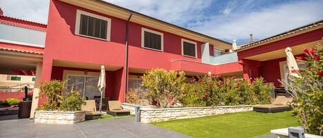 A red building with a stone patio, outdoor seating, and a well-maintained lawn.