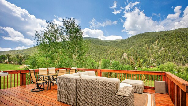A deck with wicker furniture, a wooden table, and chairs, overlooking a forested mountain range. - fishing, hot tub and room to roam! (Shawnee)