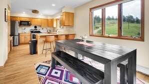 A modern kitchen with wooden cabinets, a stainless steel refrigerator, and a large window offering a view of a green landscape. - fishing, hot tub and room to roam! (Shawnee)