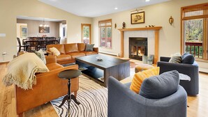 A spacious living room with a fireplace, leather sofas, a dining area, and large windows. - fishing, hot tub and room to roam! (Shawnee)