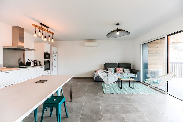 A modern kitchen with a dining area, a sofa, and a large window.