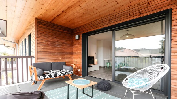 A wooden deck with a sofa, a chair, a small table, and a rug.