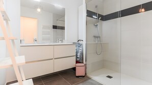 A bathroom with a shower, a mirror, a towel rack, and a suitcase.