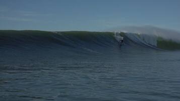 Een hoge golf in de oceaan, een surfer die erop surft.