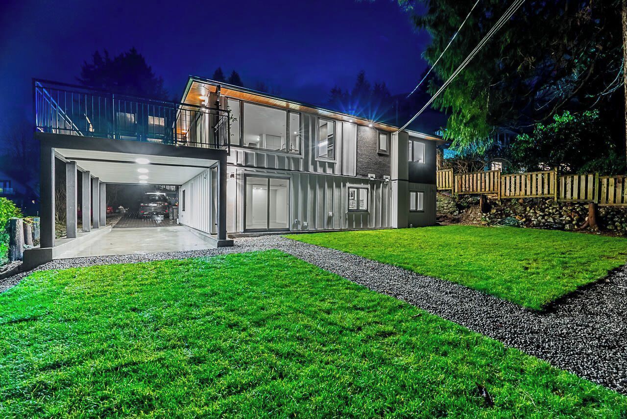 Uma casa moderna de dois andares com uma garagem grande, área externa coberta e gramado bem cuidado.