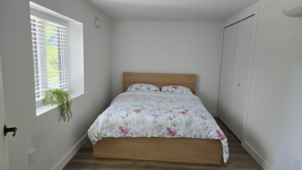 Un dormitorio con una cama de madera, ropa de cama floral, una ventana con persianas y una planta en maceta.