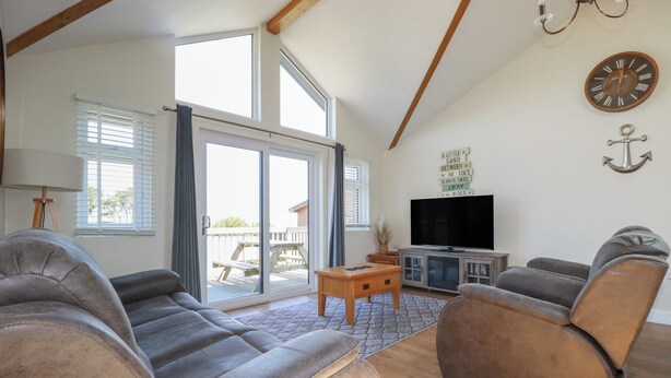 A spacious living room with a large window, a flat-screen TV, and a wooden ceiling. - Lodge 18 (Wadebridge)