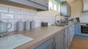 A modern kitchen with grey cabinets, a wooden countertop, a stainless steel sink, and a built-in oven. - Lodge 18 (Wadebridge)