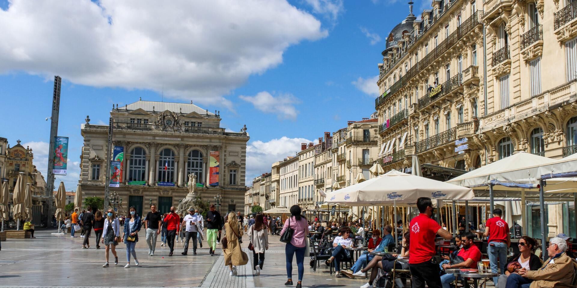 Une place animée, bordée de bâtiments historiques, avec des terrasses et une fontaine.