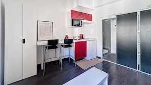 A compact kitchen with a microwave, a red cabinet, and two black chairs. - Charming Studio in Montpellier Méditerranée (Montpellier)