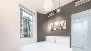 Ein modernes Schlafzimmer mit einem großen Bett, einem Fenster mit Blick auf die Stadt und abstrakter Wandkunst.