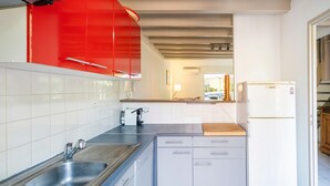 Une cuisine avec des meubles blancs, un évier en acier inoxydable, une hotte rouge et un réfrigérateur blanc.