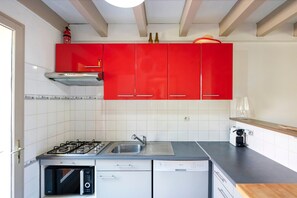 A kitchen with red cabinets, a gas stove, a microwave, and a dishwasher.