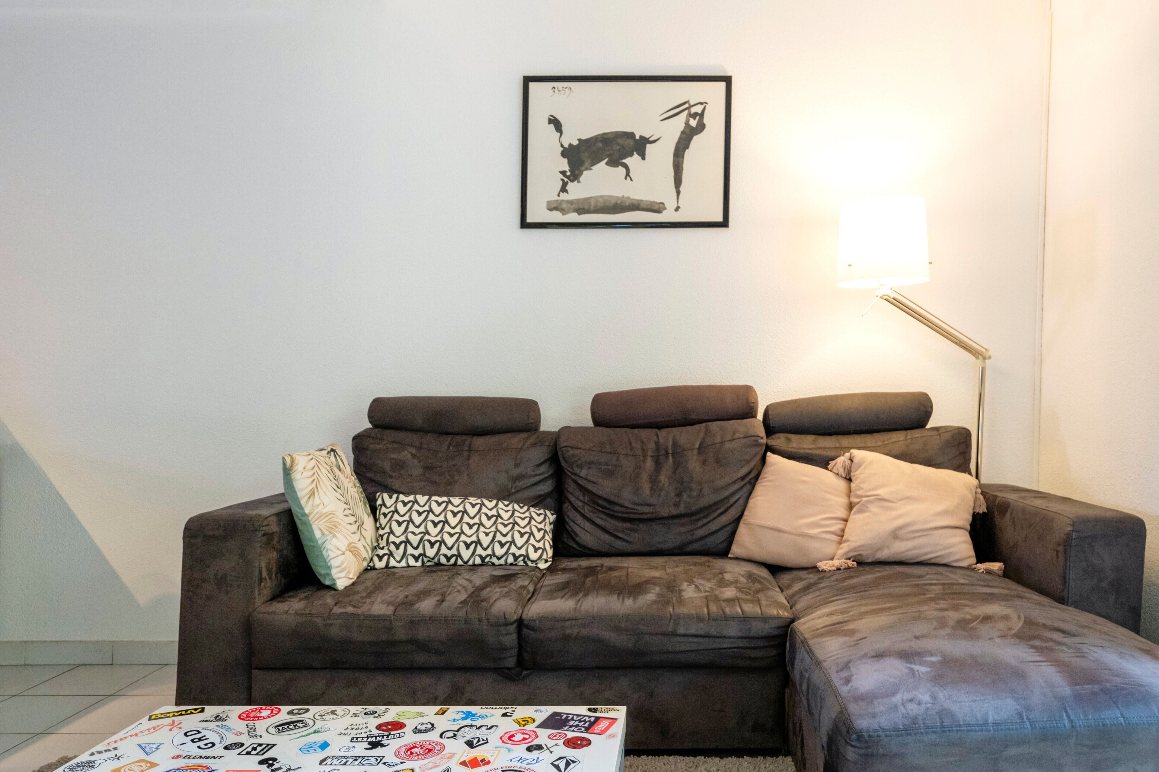 Un salon avec un canapé d’angle marron, un tableau encadré au mur et une lampe sur pied.