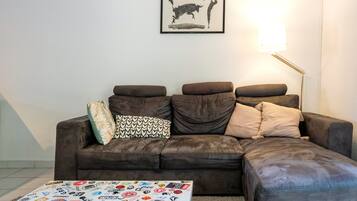 Un salon avec un canapé d’angle marron, un tableau encadré au mur et une lampe sur pied.