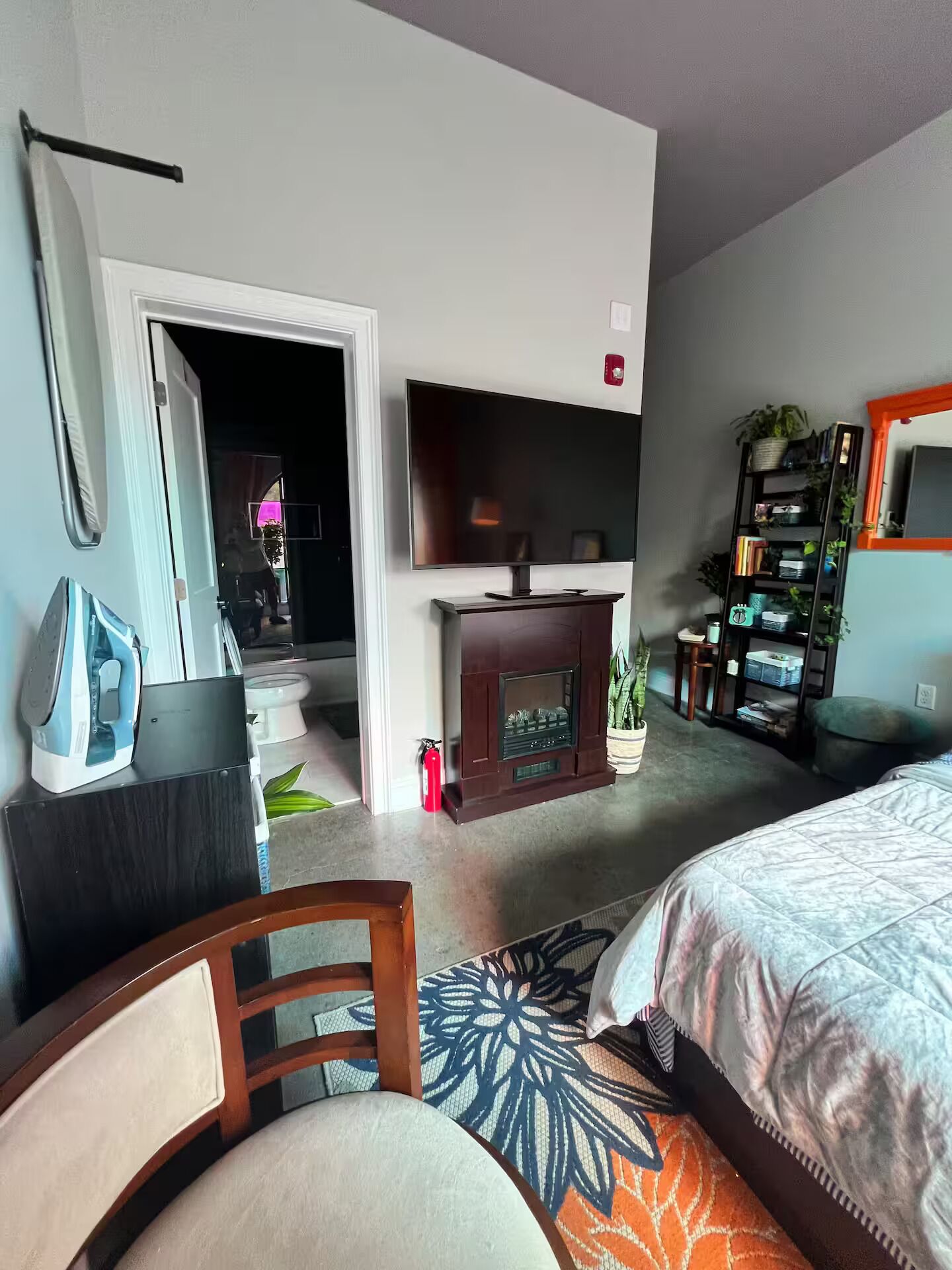 A modern bedroom with a bed, a TV, a fireplace, a bookshelf, and a door leading to another room.