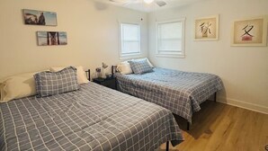 A bedroom with two beds, a ceiling fan, and artwork on the walls.
