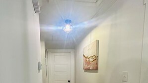 A narrow hallway with wooden flooring, white walls, and a ceiling light fixture.