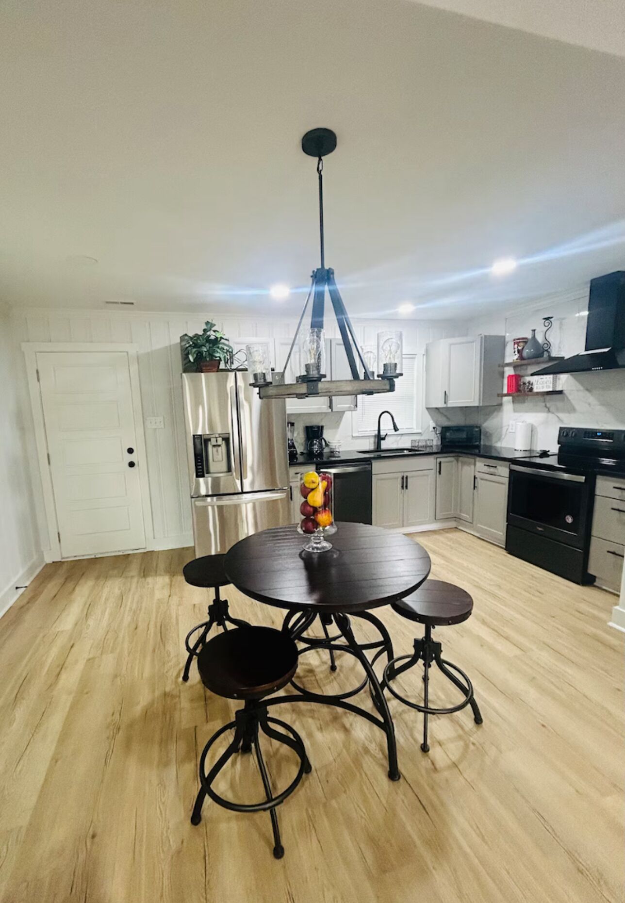 Una cocina moderna con armarios blancos, electrodomésticos de acero inoxidable y una mesa de comedor de madera con cuatro sillas.
