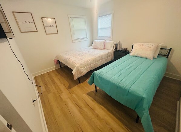 A bedroom with two beds, wooden flooring, and a window with blinds.