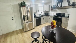 A modern kitchen with stainless steel appliances, a wooden floor, and a dining area with a table and stools.