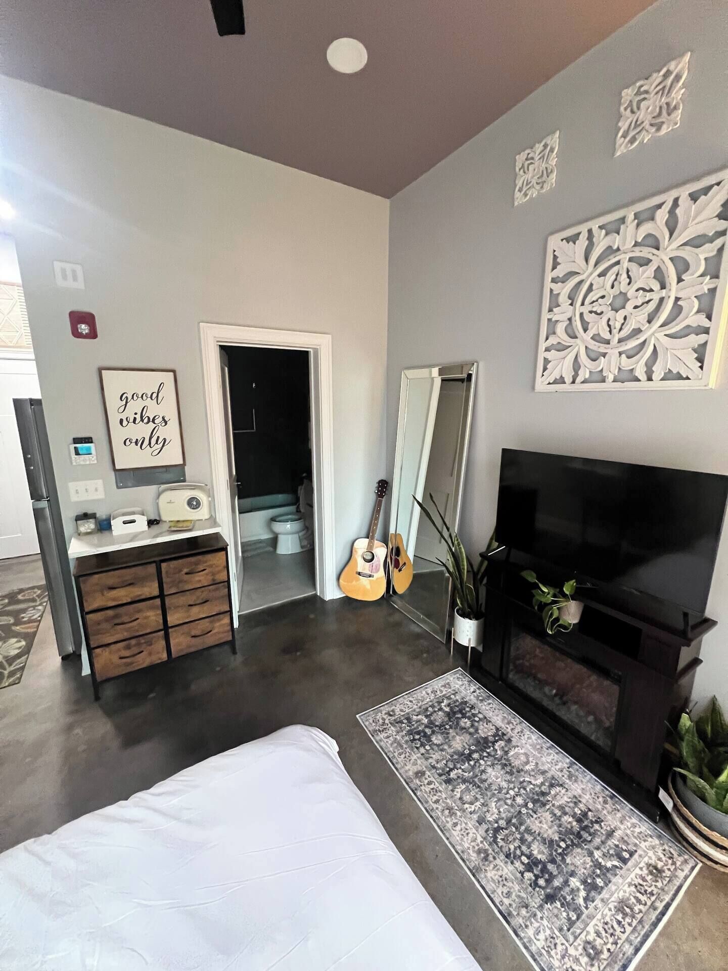 Quarto moderno com cama, televisão, cômoda e um violão.