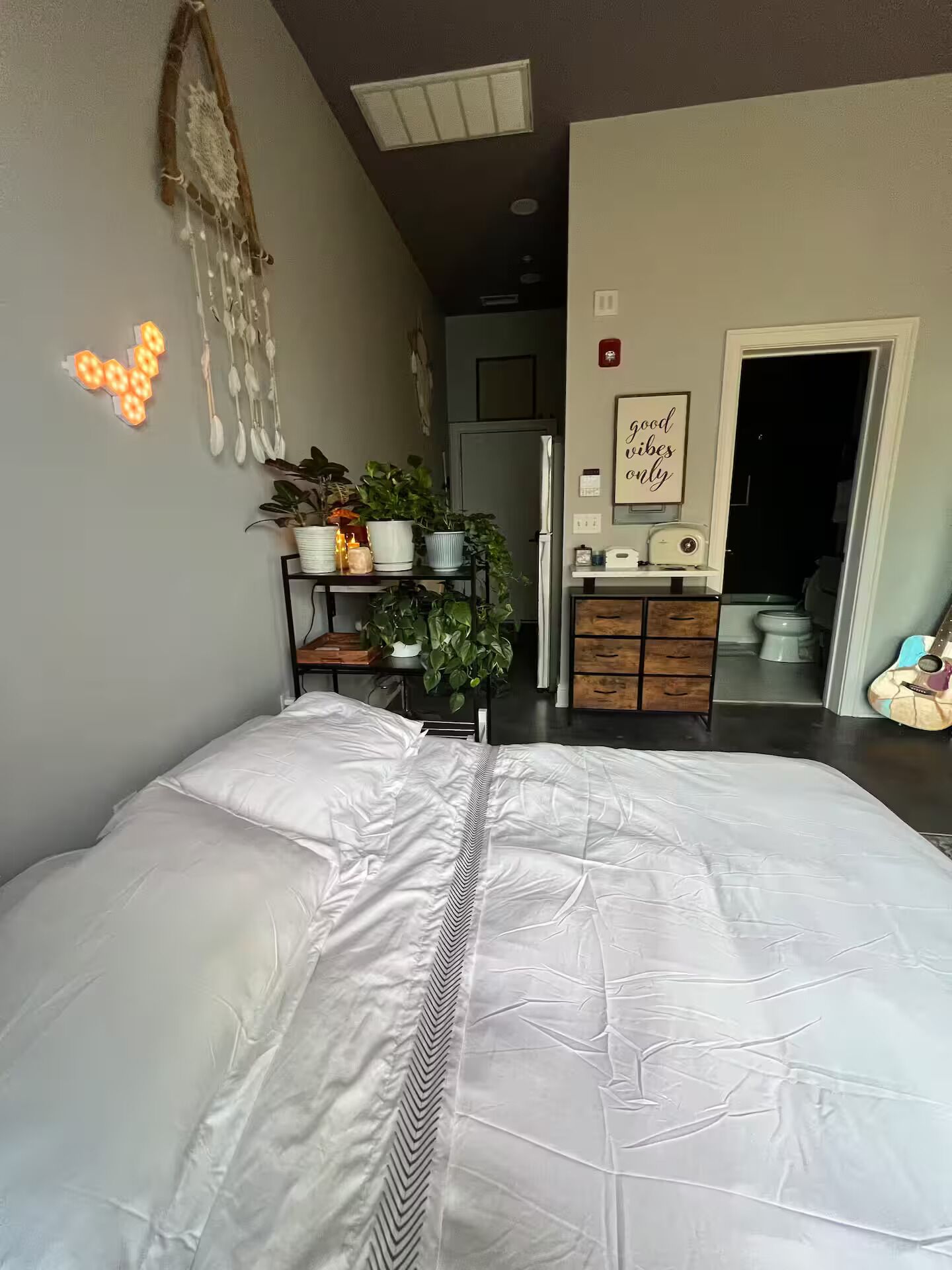 Una camera da letto con un letto grande, un comodino con una lampada, uno scaffale a parete con piante e una porta che dà su un'altra stanza.