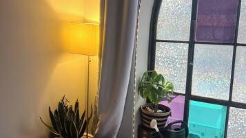 Una habitación acogedora con un ventanal curvo, una lámpara, un sofá y una mesita con plantas y un juego de mesa.