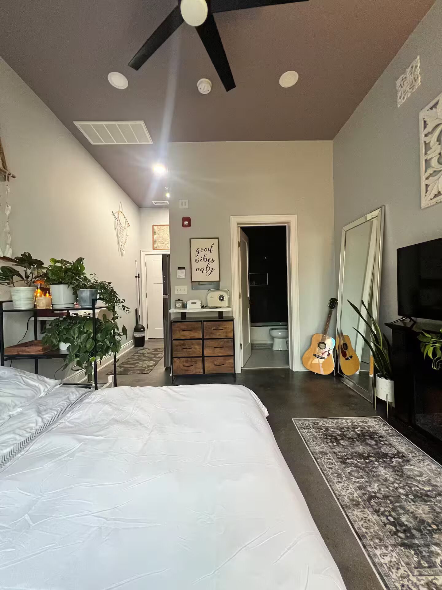 Ein Schlafzimmer mit Bett, Deckenventilator, Kommode, Gitarre und Fernseher.