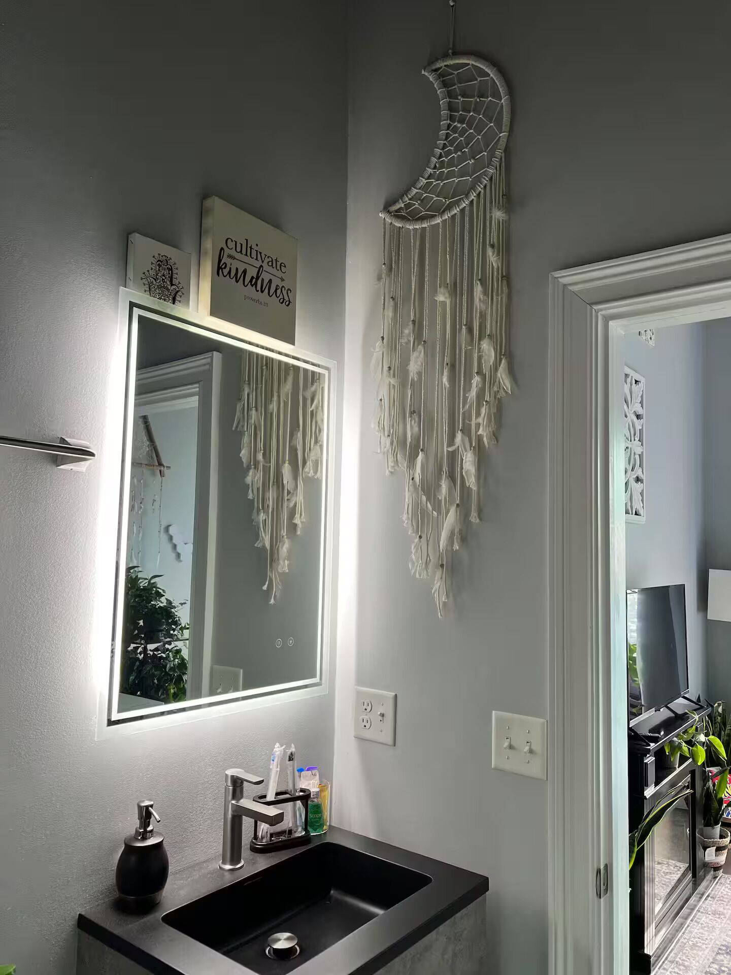 Een badkamer met een grote spiegel, een wastafelmeubel met een wastafel en een dromenvanger aan de muur.
