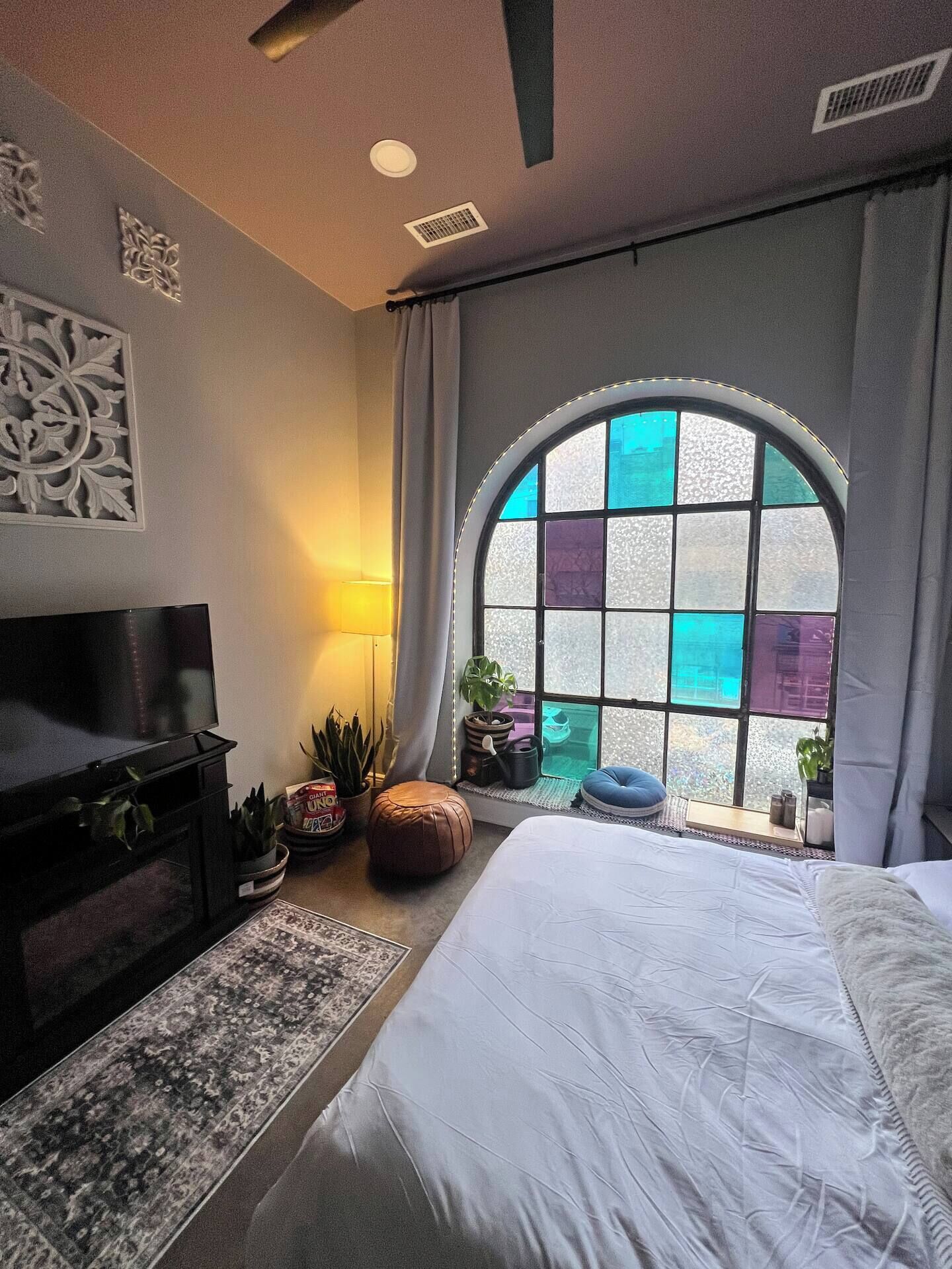A bedroom with a large bed, a TV, a window with a view, and a decorative wall piece.