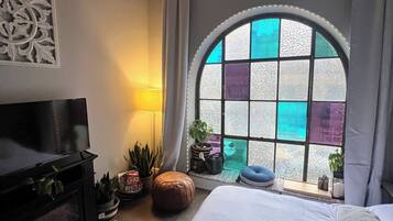 A bedroom with a large bed, a TV, a window with a view, and a decorative wall piece.