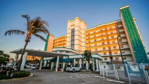A multi-story hotel with a curved facade, a covered entrance, and a parking area. - Family Escape | Oceanfront Condo + Pool Access (Cocoa Beach)