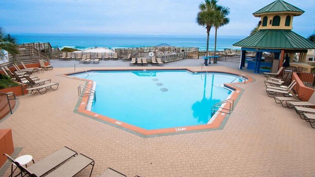 A pool area with lounge chairs, a small gazebo, and a view of the ocean.
