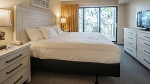 Ein Hotelzimmer mit einem Bett, einem Fernseher, einem Schreibtisch mit Lampe, einem Telefon und einem Fenster mit Vorhängen.